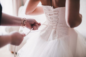 Hochzeitskleider im Hintergrund im Vordergrund wird der Braut ins Hochzeitskleid geholfen